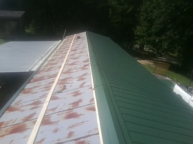 Old rusted panels beside newly installed green metal roofing — Wind Damage Roof Repair by Roofing Brothers in Leola